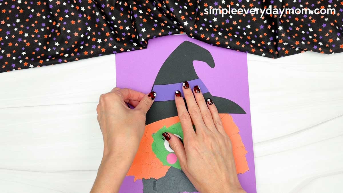 Hands gluing a purple hat band across the black witch hat for the Witch Torn Paper Craft.