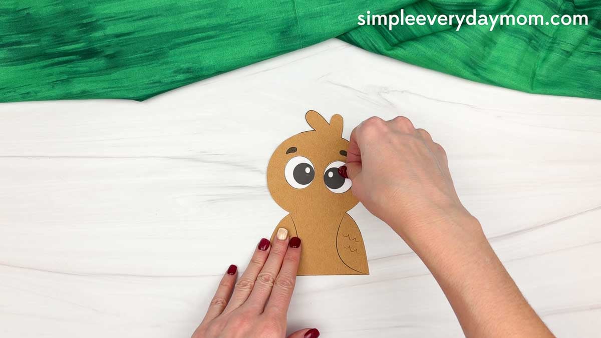 Hands gluing the eyes onto a brown paper turkey for a fun fall turkey craft for kids.