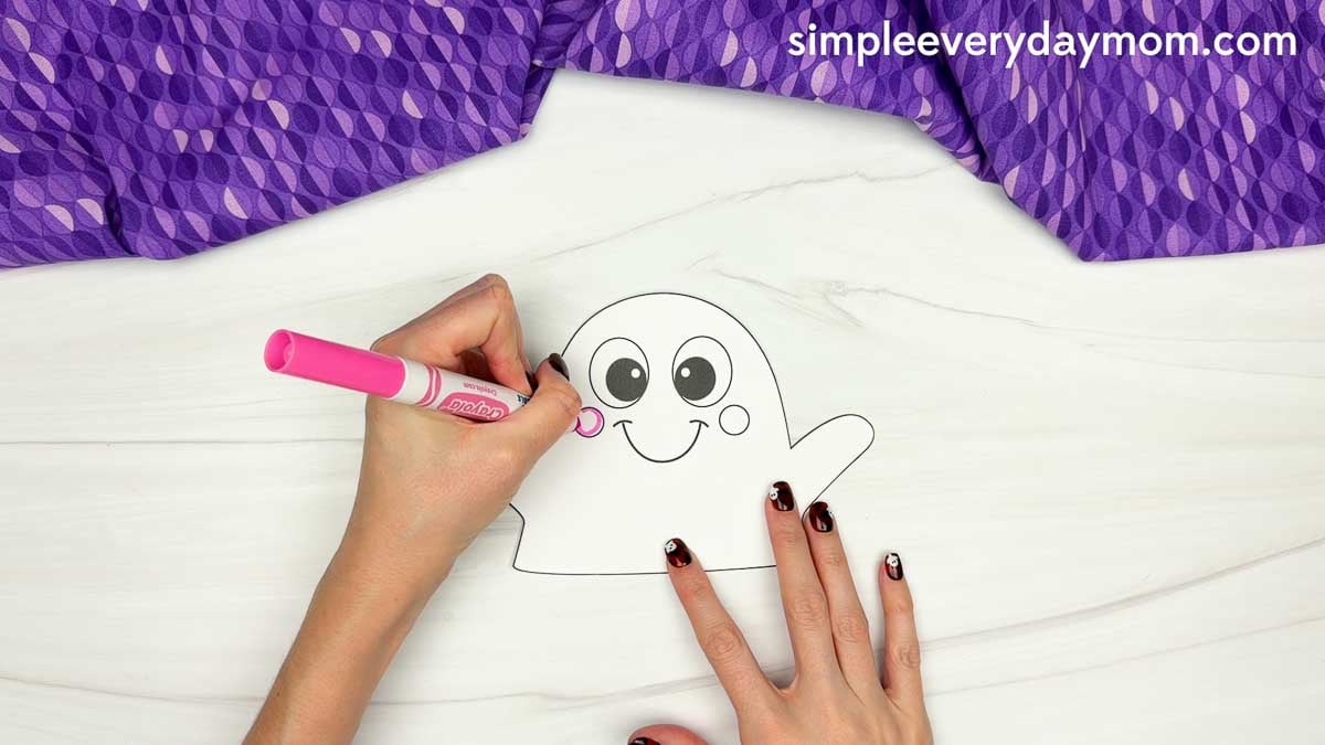 Hands coloring the cheeks of a clown ghost disguise craft with a pink marker.
