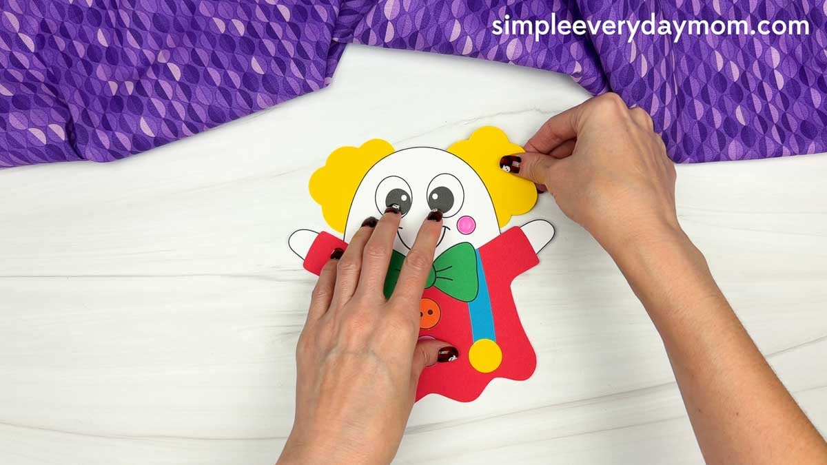 Hands attaching yellow clown hair to both sides of the head on a clown ghost disguise craft.