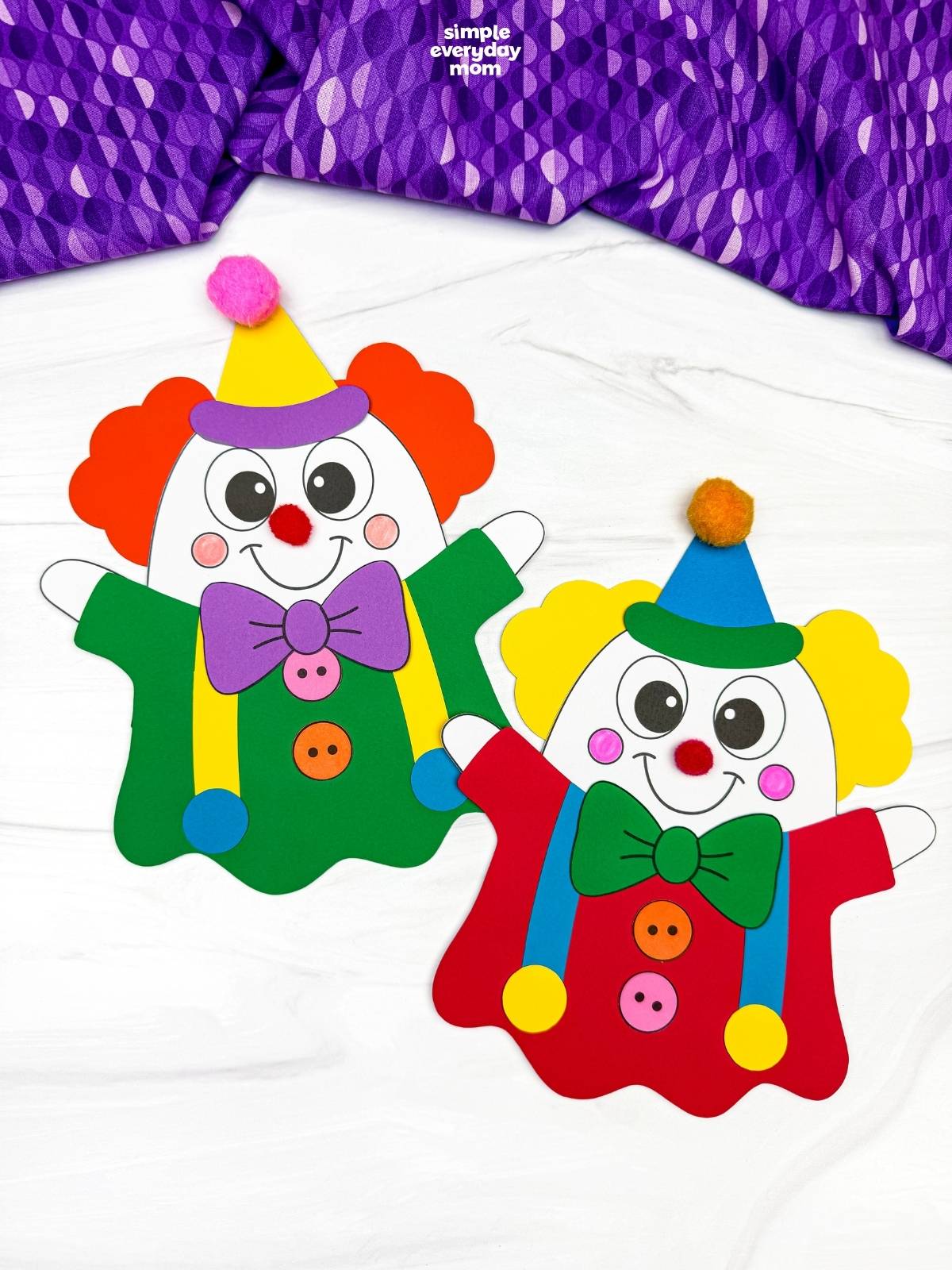 A completed craft display of two clown ghost disguises with colorful outfits, bow ties, party hats, and pom-pom noses for a fun Halloween activity for kids.