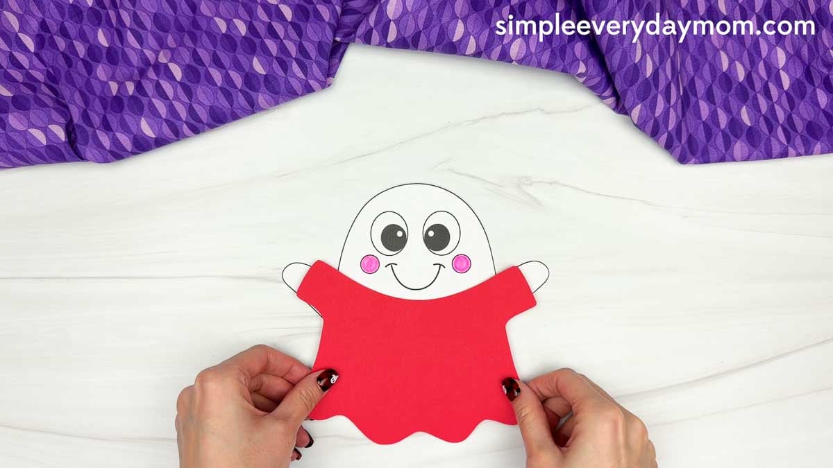 Hands positioning the red body piece over the clown ghost disguise craft with pink cheeks.