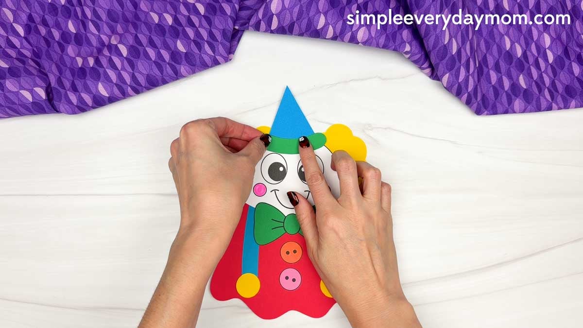 Hands attaching the green hat brim to the blue party hat on a clown ghost disguise craft.