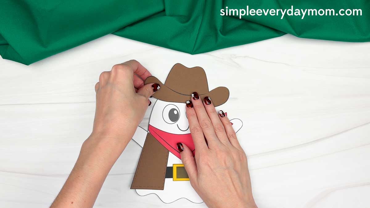 Hands gluing the cowboy hat onto the top of the ghost’s head for the Cowboy Ghost Disguise Craft.
