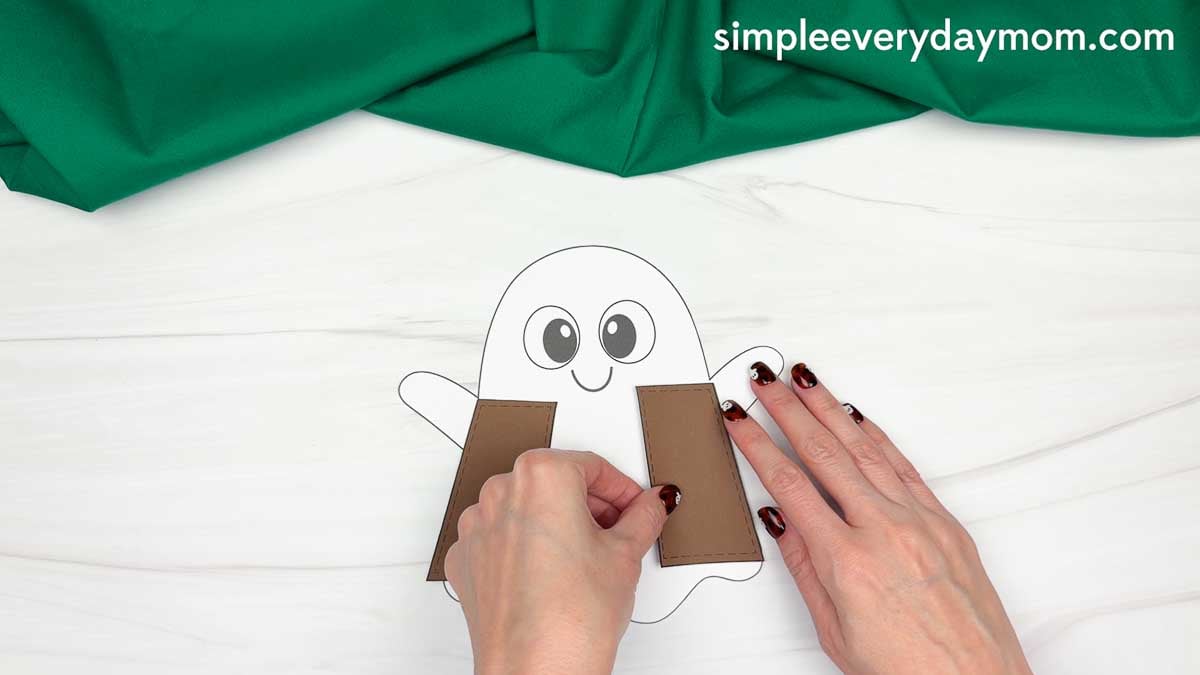 Hands gluing the two vest pieces onto the sides of the ghost for the Cowboy Ghost Disguise Craft.