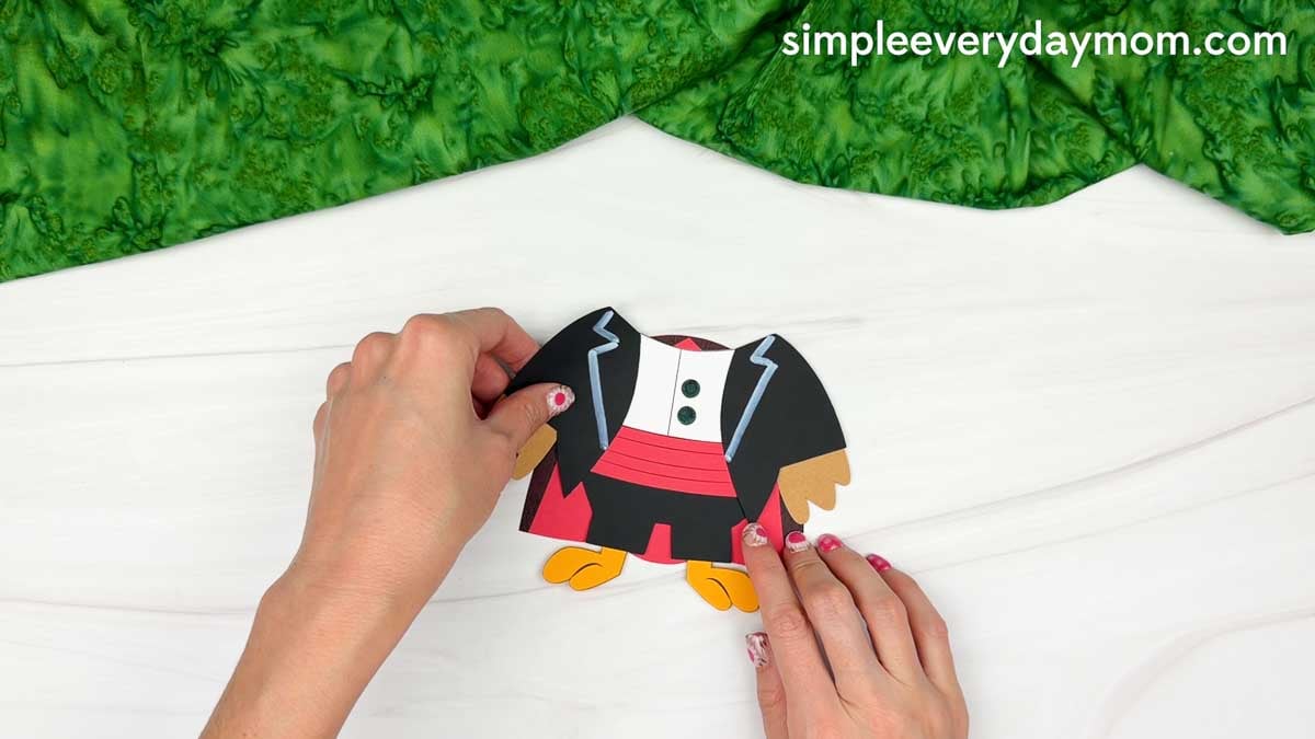 Hands attaching the red and black magician's cape behind the turkey's body for the Magician Turkey Disguise Craft.