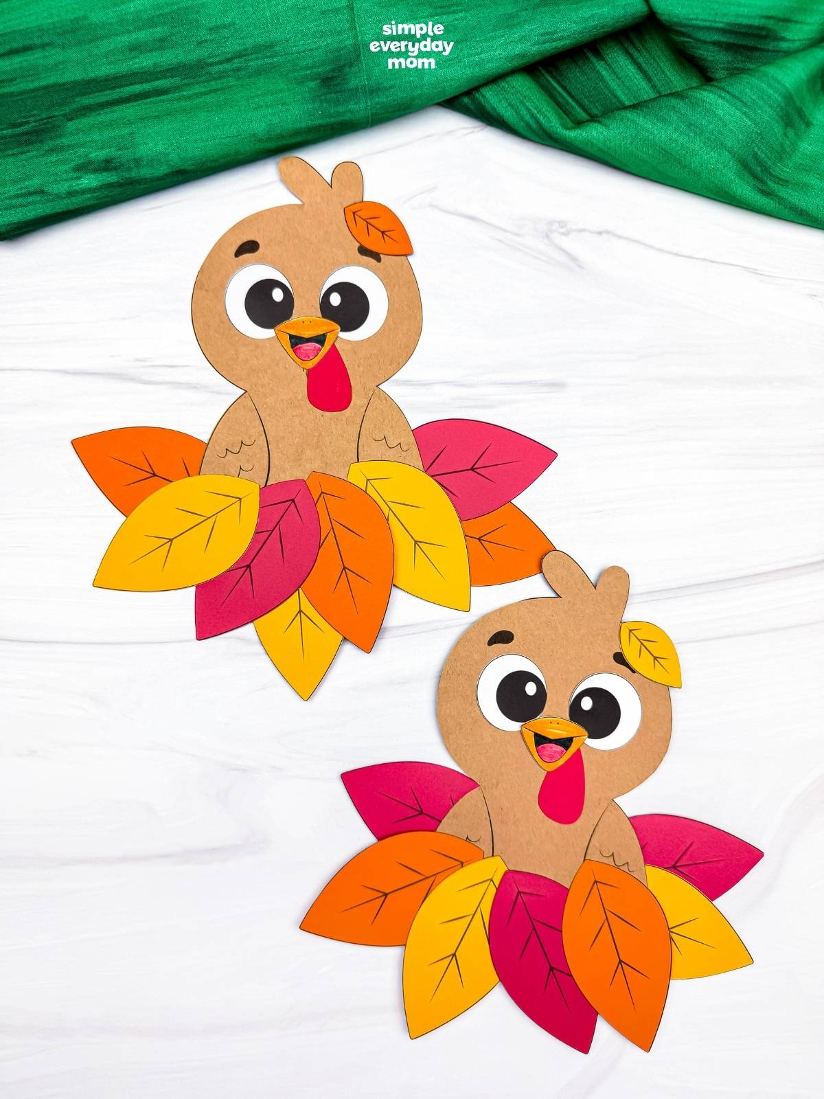 A completed craft featuring two cute brown paper turkeys nestled in colorful fall leaf piles for a fun Thanksgiving activity for kids.
