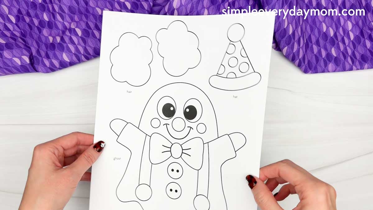 Hands holding a printable clown ghost disguise craft template featuring a ghost, clown hair, and party hat.