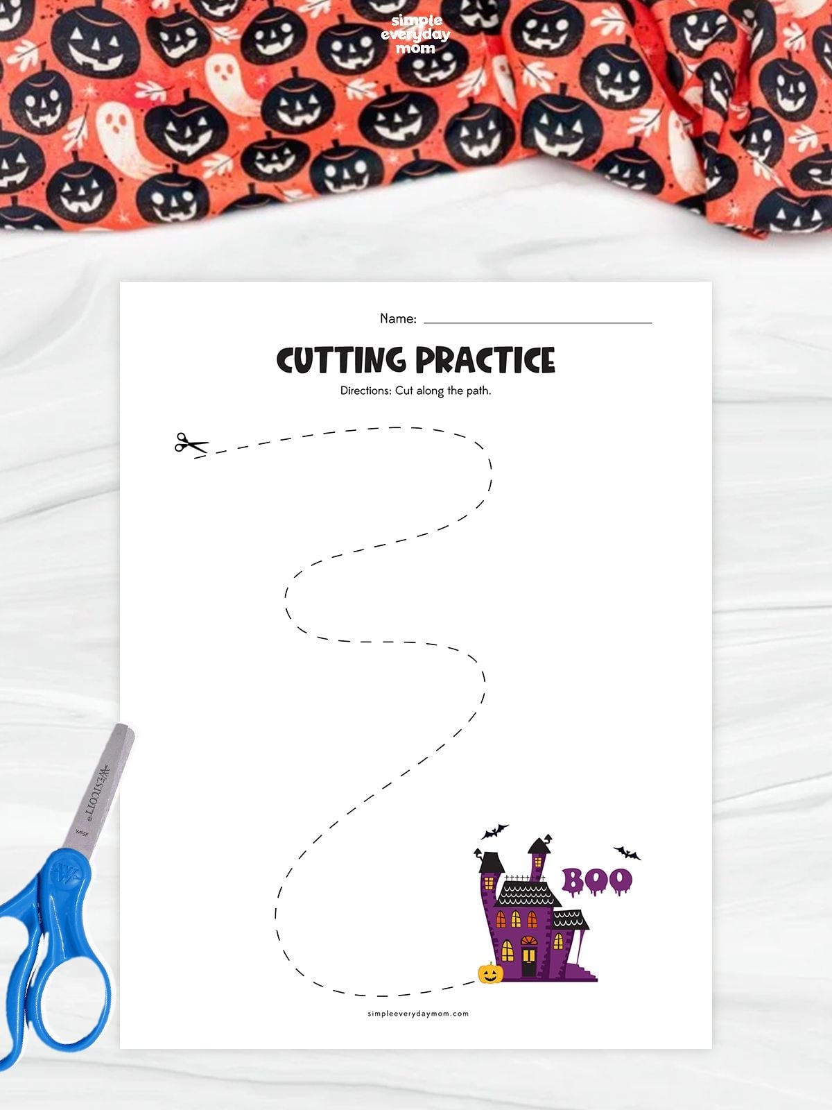Printable Halloween cutting practice worksheet featuring a winding dashed path leading to a haunted house with bats and a pumpkin, helping preschoolers develop scissor control and fine motor skills.