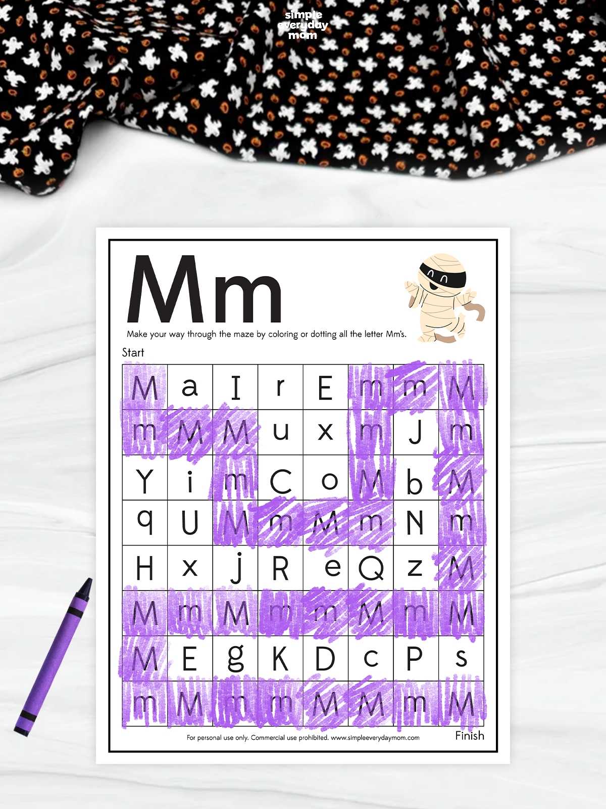 A printable Halloween letter M maze worksheet featuring a cute mummy and purple-colored uppercase and lowercase M letters for preschool and kindergarten letter recognition activities.