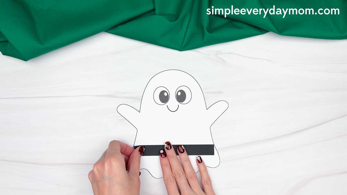 Hands gluing the belt piece across the bottom of the ghost for the Cowboy Ghost Disguise Craft.