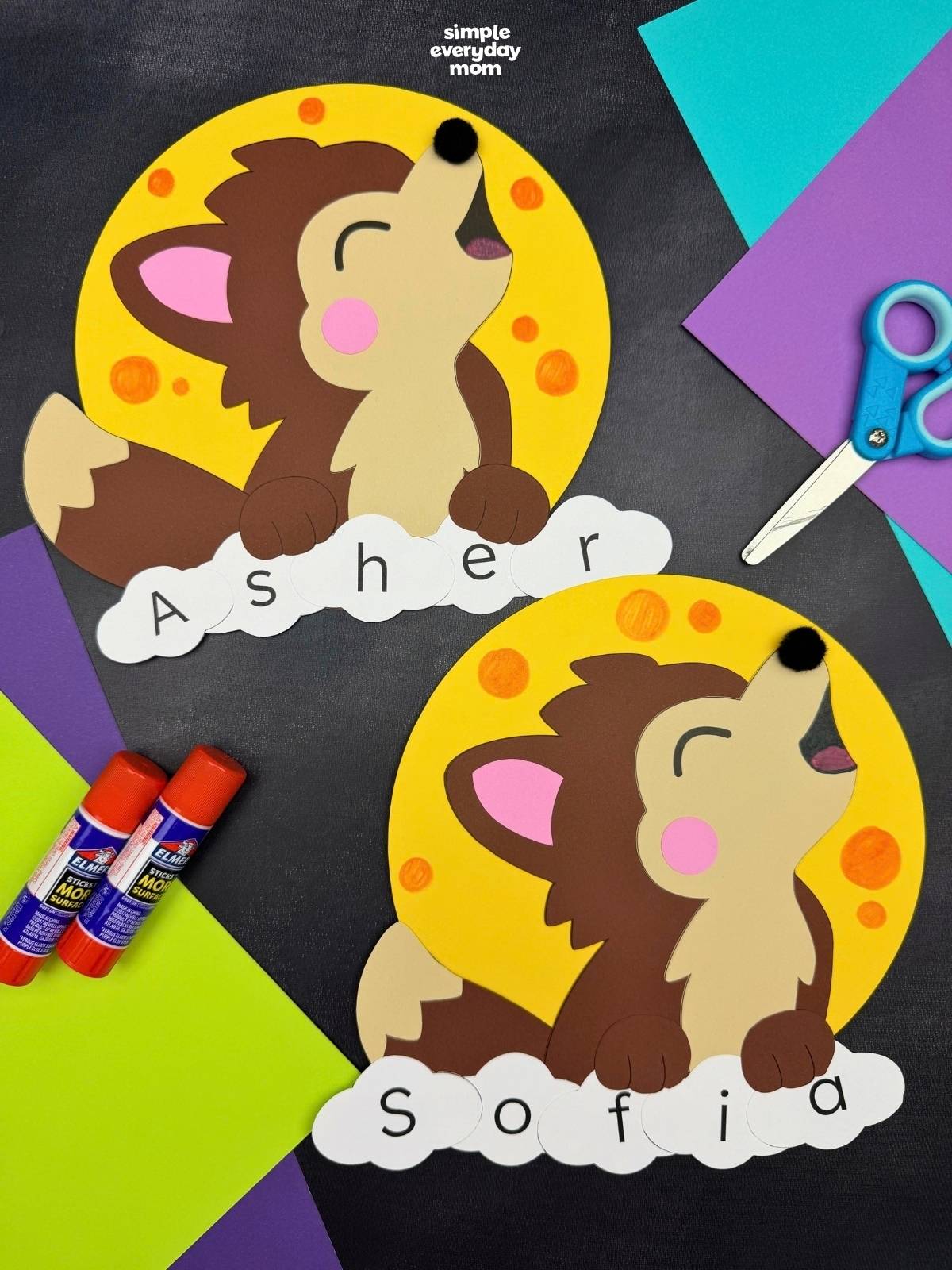 A completed craft featuring two werewolf name projects with yellow full moons and lettered pieces spelling children's names, surrounded by colorful paper and craft supplies.