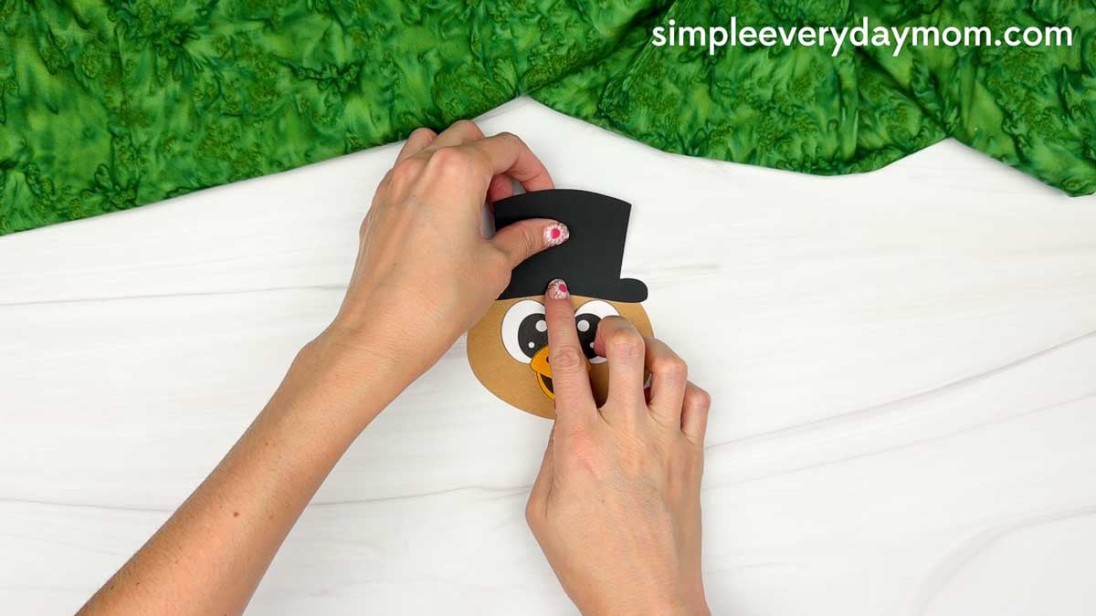 Hands gluing a black magician's top hat onto the turkey's head for the Magician Turkey Disguise Craft.
