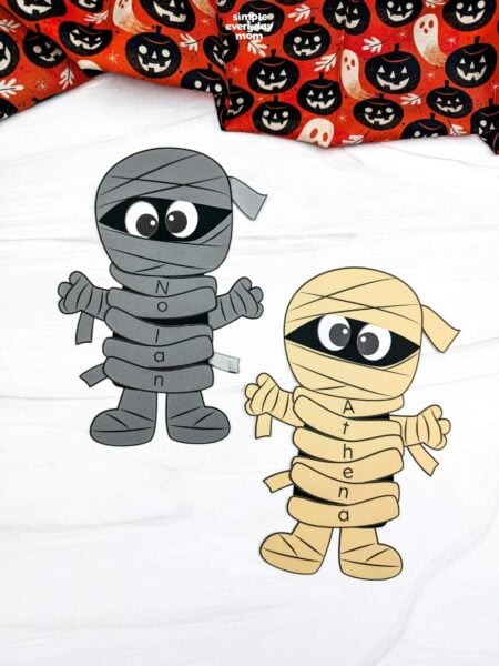 A completed craft showing gray and yellow mummy name crafts with personalized lettered wraps spelling Nolan and Athena for a fun Halloween name recognition activity for kids.