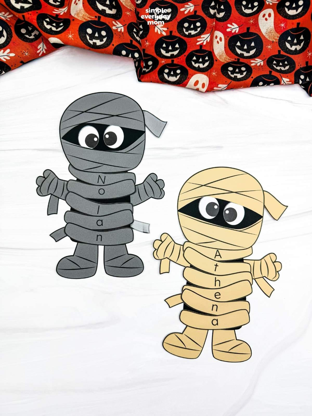 A completed craft showing gray and yellow mummy name crafts with personalized lettered wraps spelling Nolan and Athena for a fun Halloween name recognition activity for kids.