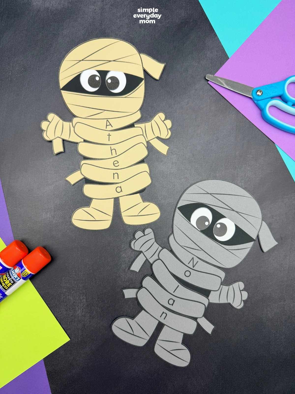 A completed craft featuring two personalized mummy name crafts with lettered wraps on a black background, perfect for a Halloween name recognition activity for kids.