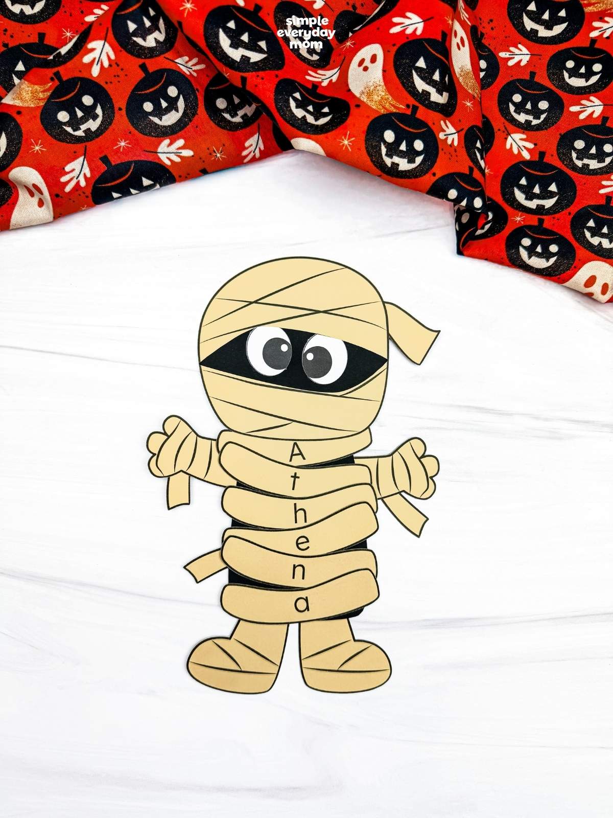 A completed craft showing a yellow mummy name craft with lettered wraps spelling Athena, perfect for a Halloween name recognition activity for kids.