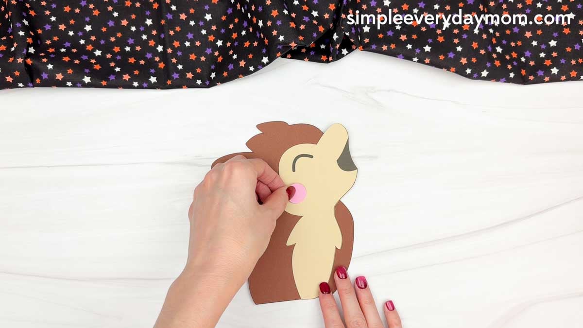 Hands gluing a pink cheek onto the werewolf's face for a Halloween name craft.