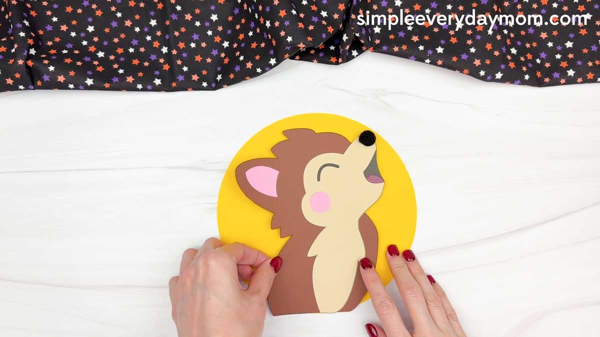 Hands gluing the werewolf onto a yellow full moon background for a Halloween name craft.