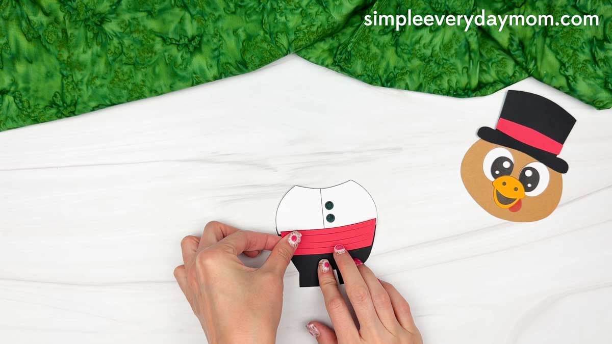 Hands gluing a red striped waistband across the black body below the white shirt for the Magician Turkey Disguise Craft.