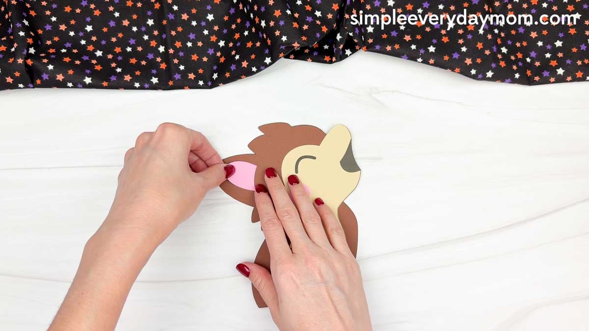 Hands gluing the pink inner ear onto the werewolf's ear for a Halloween name craft.