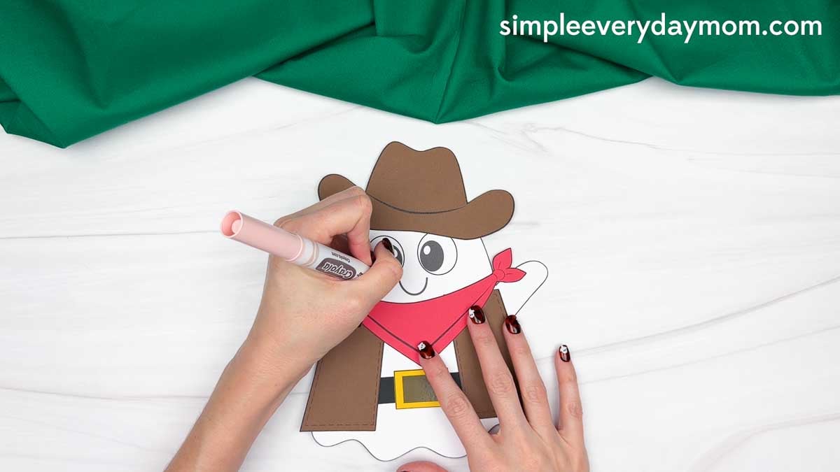 Hands adding details to the ghost’s face with a marker after attaching the cowboy hat, bandana, vest, belt, and buckle.