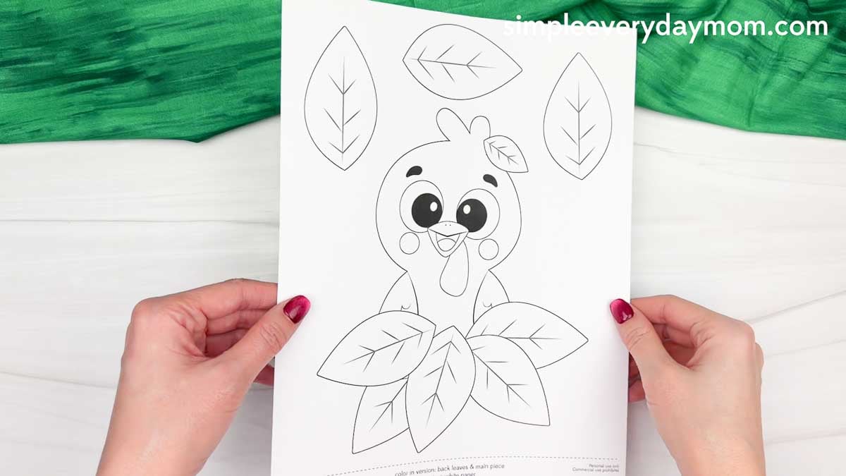 Hands holding a printable Fall Turkey Craft template featuring a cute turkey and autumn leaf pieces ready to color and cut out.