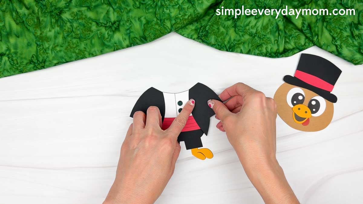 Hands attaching the black jacket pieces to both sides of the turkey's body for the Magician Turkey Disguise Craft.