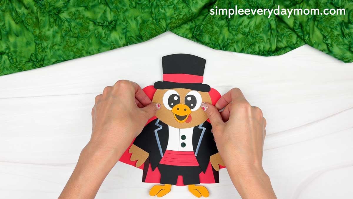 Hands attaching the turkey's head above the black magician's jacket, centered over the body for the Magician Turkey Disguise Craft.