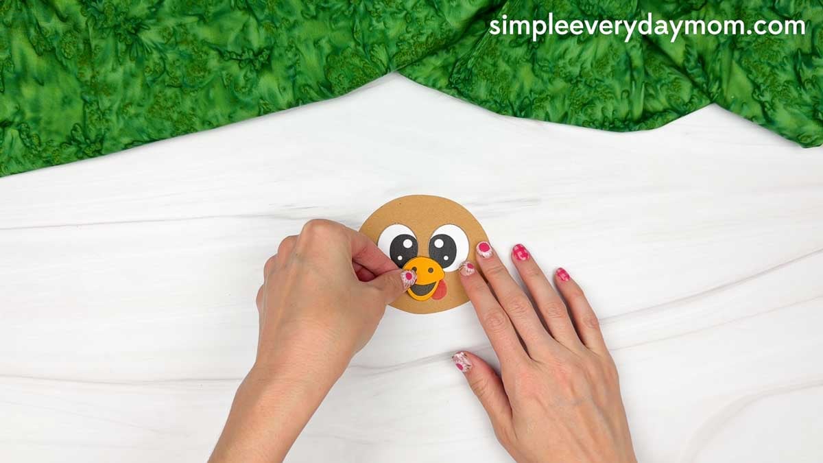 Hands placing the orange beak above the smiling mouth on the turkey's head for the Magician Turkey Disguise Craft.