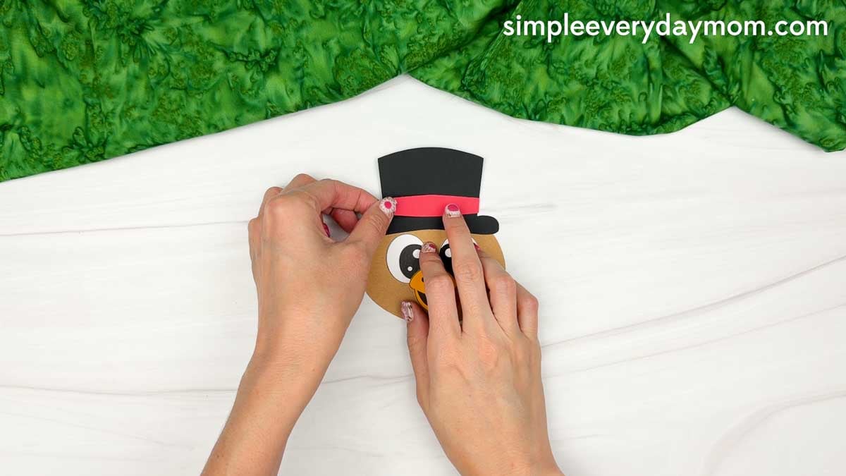 Hands attaching a red hatband across the black top hat on the turkey's head for the Magician Turkey Disguise Craft.